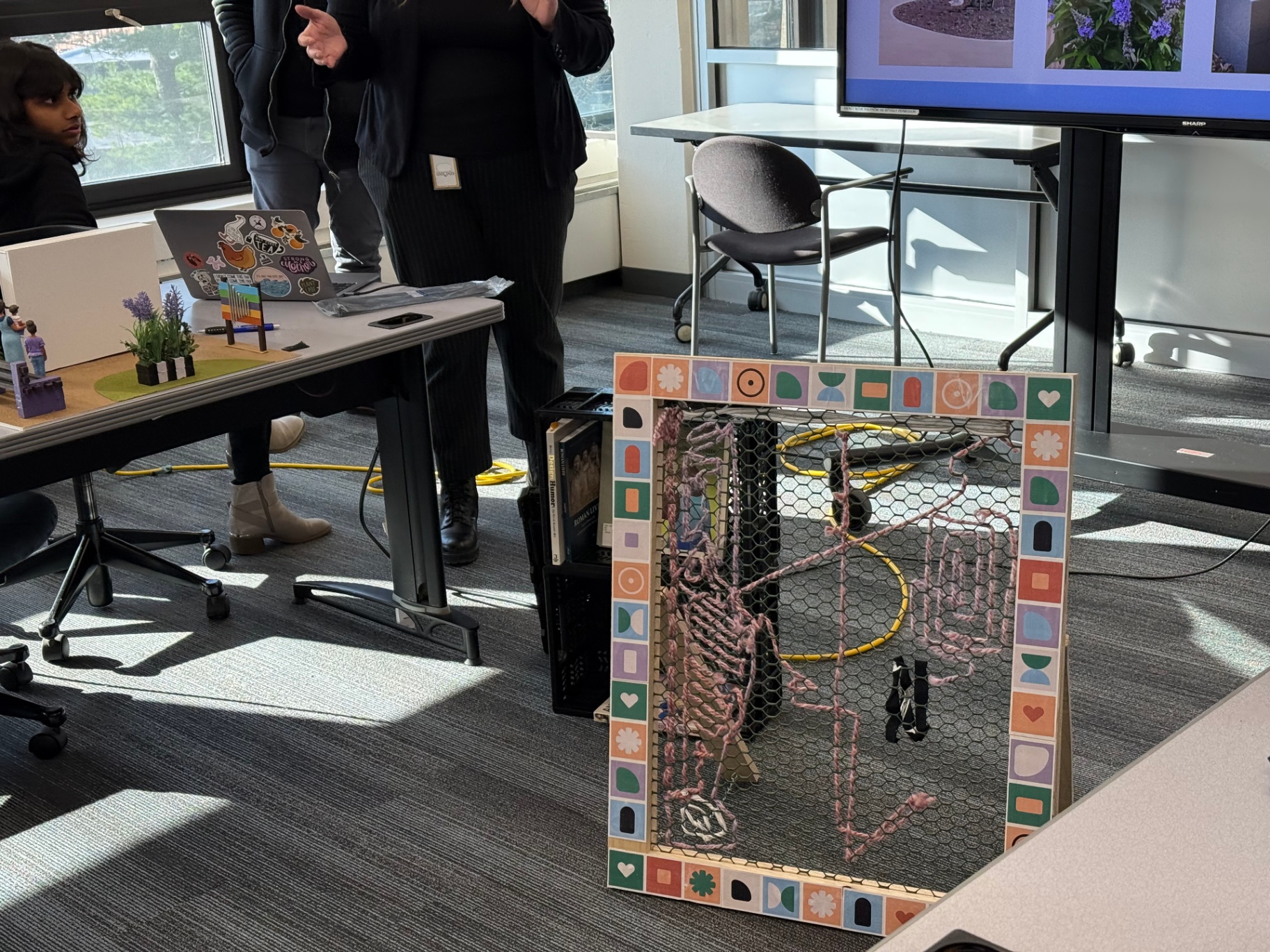 Mixed-media artwork using chicken wire, yarn, and patterned border tiles